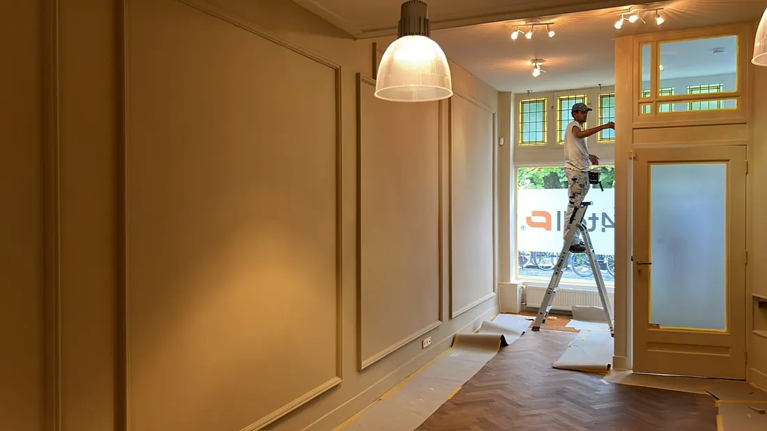 Schilder op een trap in een winkelpand met lijstwerk op de wanden